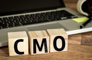 CMO (Chief Marketing Officer) written on a wooden cube in front of a laptop