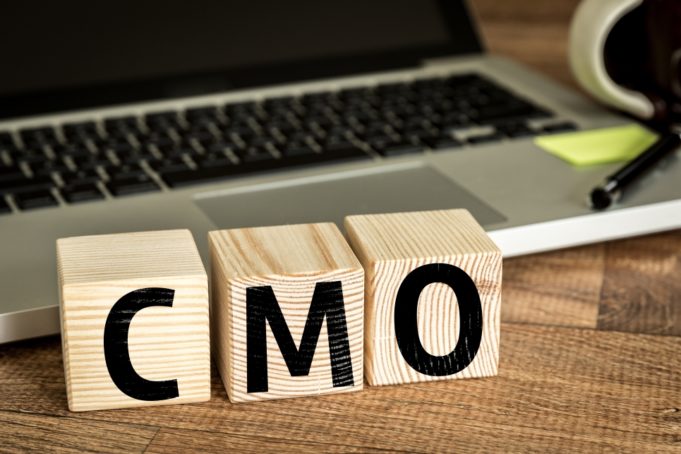 CMO (Chief Marketing Officer) written on a wooden cube in front of a laptop